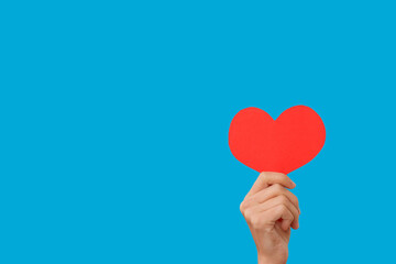 Female hand holding a heart - a symbol of love, isolated blue background