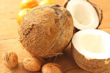 a whole coconut and a sliced coconut on a wooden table with oranges