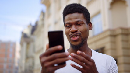 Excited afro guy having video call on street. Man making hand gesture outdoors