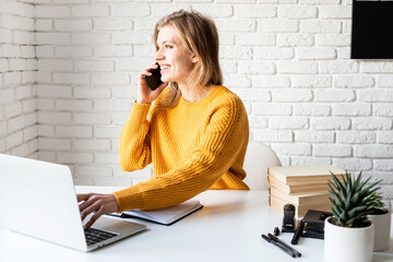 Young woman in yellow sweater using laptop and calling on the phone