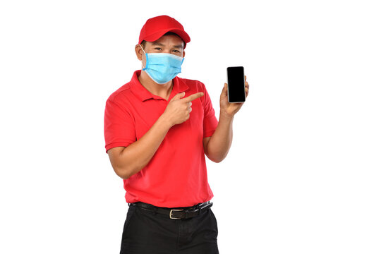 Young Asian delivery man in red uniform, medical face mask, protective gloves holding and introducing use of smart phone for delivery isolated on white background