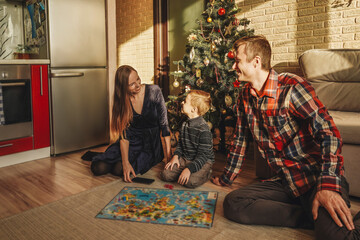 Happy family playing board game walker at home, christmas tree on background. Holidays home.