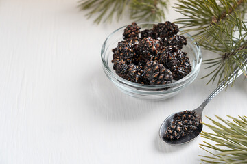 Siberian healthy dessert of dried pine cones preserved in sweet syrup served in bowl on white wooden background with spoon and pine branches at winter holidays at kitchen. Image with copy space