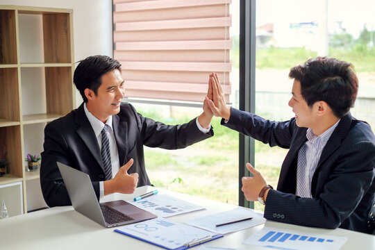 Happy young asian businessman successful  giving a high fives showing cooperation and success at work.