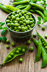 Fresh green peas in a small metal bucket on old wooden background.