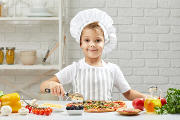 smiling little boy in chef hat and an apron cooking pizza in the kitchen.