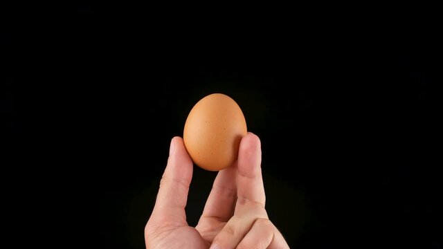 Holding an egg in her hands. Black background. Close up
