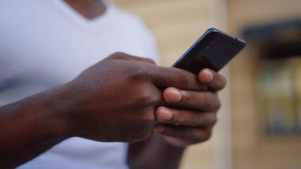 Unknown afro guy texting message on street. African man hands with mobile phone