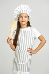 cute little girl in chef hat and apron on gray background. child dreams of becoming a chef