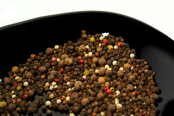 Peppercorns on a black shiny plate close up on a white background