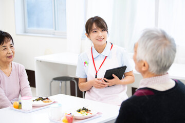 食事中の高齢の入居者たちと介護施設の女性職員