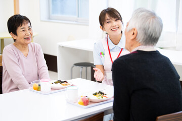 食事中の高齢の入居者たちと介護施設の女性職員