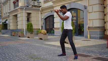Energetic guy dancing latino dance on street. Man making dance elements in city