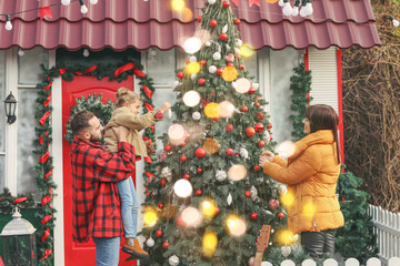 Happy family decorating Christmas tree near house outdoors