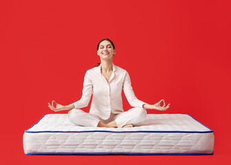 Young woman meditating on mattress against color background