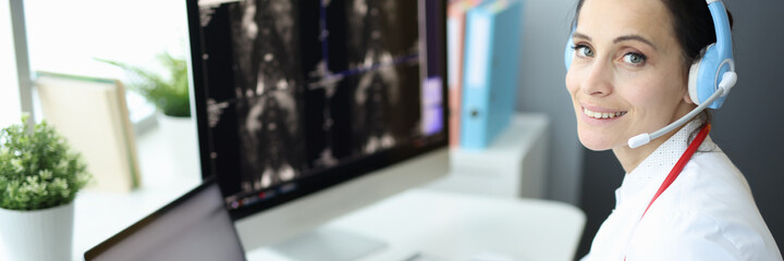 Medical officer is at computer wearing headphones and holding an X-ray. Online medical help from...