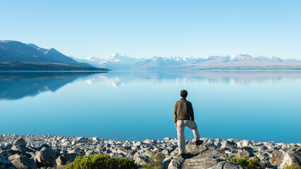 Fototapeta na wymiar Tourist standing on the shore of Lake Pukaki, watching Mt Cook reflected in the clear waters