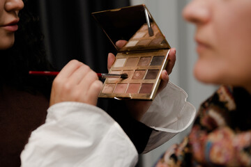 Make up. Young beautiful woman, makeup artist holding a brush and shadows, in the beauty studio...