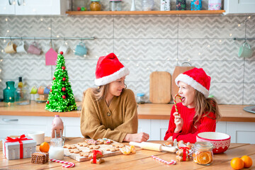 Little girls making Christmas gingerbread house at fireplace in decorated living room.