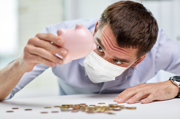 business, finances and health concept - businessman wearing face protective medical mask for protection from virus disease shaking piggy bank and getting coins at office