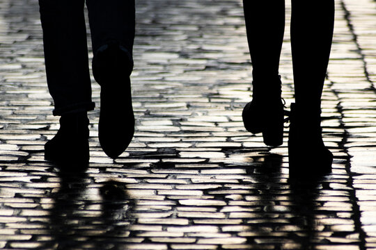 Dark Silhouettes And Shadows Of People On Sidewalk. Two Pedestrians Walking Down On Evening Street. Soft Focus, Shallow Depth Of Field.