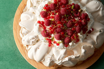food, culinary, baking and cooking concept - close up of pavlova meringue cake decorated with red berries on wooden serving board