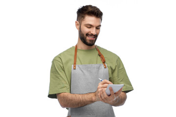 people, profession and job concept - happy smiling waiter in apron taking notes to notepad over white background