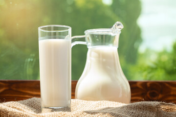 Pitcher of milk on wooden table against blurred foliage background
