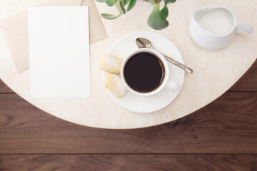 A cup of coffee with cookies, a silver spoon, milk, an empty letterhead with an envelope on a marble table in a cafe. Top view