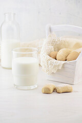 Bottle, glass of milk and homemade cookies in a white vintage basket with a linen napkin on a wooden table. Home furnishings