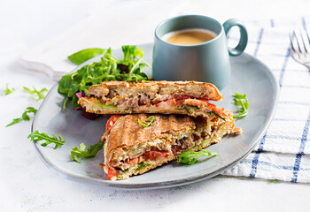 Grilled club sandwich panini with beef, tomato, cheese, lettuce and cup of coffee. Delicious breakfast or snack.
