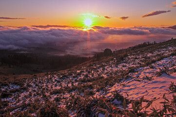 冬の朝の峠からの風景。太陽の光と眼下を覆う雲。