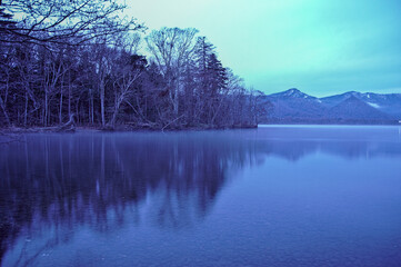  雲の漂う空と湖畔の森を水面に映す湖

