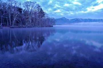 雲の漂う空と湖畔の森を水面に映す湖