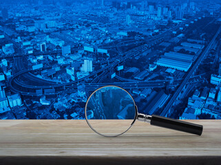 Magnifying glass on wooden table over modern office city tower, street, expressway, and skyscraper, Business analyzing concept