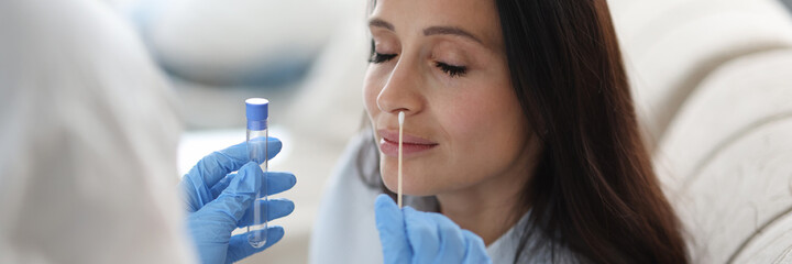 Doctor laboratory assistant in protective suit takes swab from nose of sick patient at home....