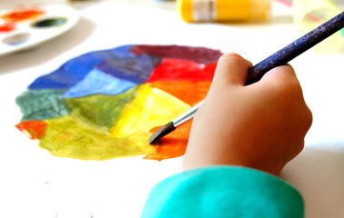 Close-up of childs hand with drawing by brush and gouache paints. Children create artist paints creativity vacation, training, drawing, coloristic courses, painting, color science.