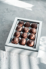 Handmade assorted chocolate truffle candies in box on white stone background. Silver box in sunbeams