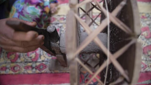 A female hand turning traditional Indian spinning wheel to make cotton threads. Manual labor for Indian organic clothing industry in a small textile factory in Rajasthan, India. Slow motion, 4K.