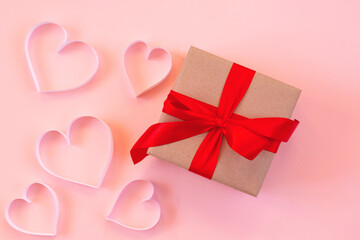 Paper cut hearts, gift box with red bow on pastel pink background. Composition for Valentine's Day, postcard. Flat lay, top view, copy space.