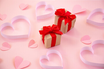 Paper cut hearts, gift box with red bow on pastel pink background. Composition for Valentine's Day, postcard. Flat lay, top view, copy space.