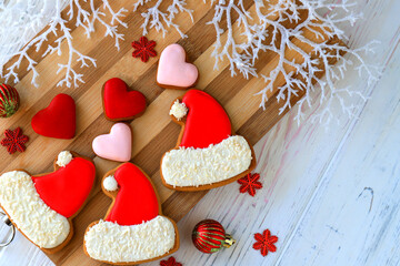 Christmas cookies, gingerbread cookies in the form of red Santa Claus cap and heart with icing lie among the New Year decorations on wooden background. Festive homemade food