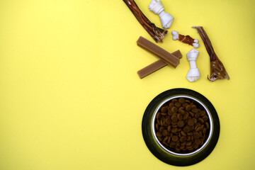 Dog treats and dry feed in bowl on yellow background with copy space. Variety of dog treats. flat lay