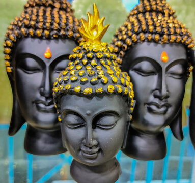 Front view of a Statue of closed eyes child form of buddha carved out of black rock. Statue of Adult buddha in background.