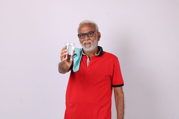 senior indian man holding glass of water while or after weight training or gym, keeping himself dehydrated