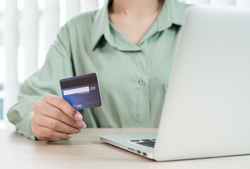 The businesswoman's hand is holding a credit card and using a laptop for online shopping and internet payment in the office