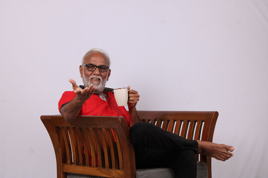 Indian Old Man Reading Magazine While Sitting On Chair With A Coffee Mug.