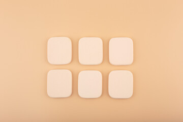 Two rows of square beige make up sponges on beige background