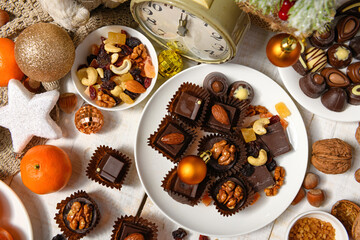 sweet food background for christmas or holiday decoration - chocolate candies, tangerines, nuts and dried fruits on white wood