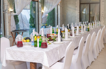 Banquet table with white tablecloth, food and drinks, white chairs